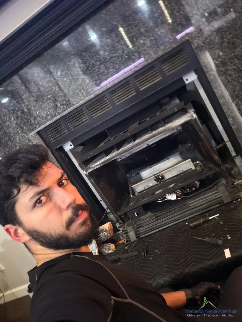Genesis technician servicing gas fireplace blower on dark marble surround
